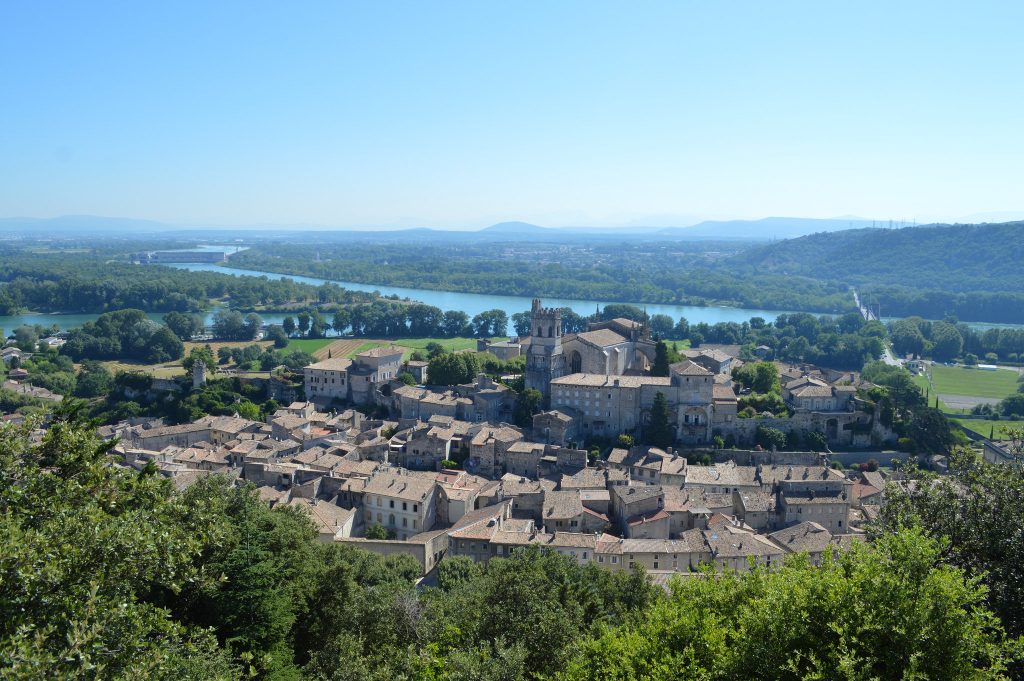 Vue panoramique du village historique de Mas Saint Antoine, avec ses bâtiments en pierre et sa grande église, entouré de verdure et d’arbres luxuriants, d’une rivière sinueuse, de montagnes au loin et d’une piscine étincelante sous un ciel bleu limpide. Vue panoramique du village historique de Mas Saint Antoine, avec ses bâtiments en pierre et sa grande église, entouré de verdure et d'arbres luxuriants, d'une rivière sinueuse, de montagnes au loin et d'une piscine étincelante sous un ciel bleu limpide.