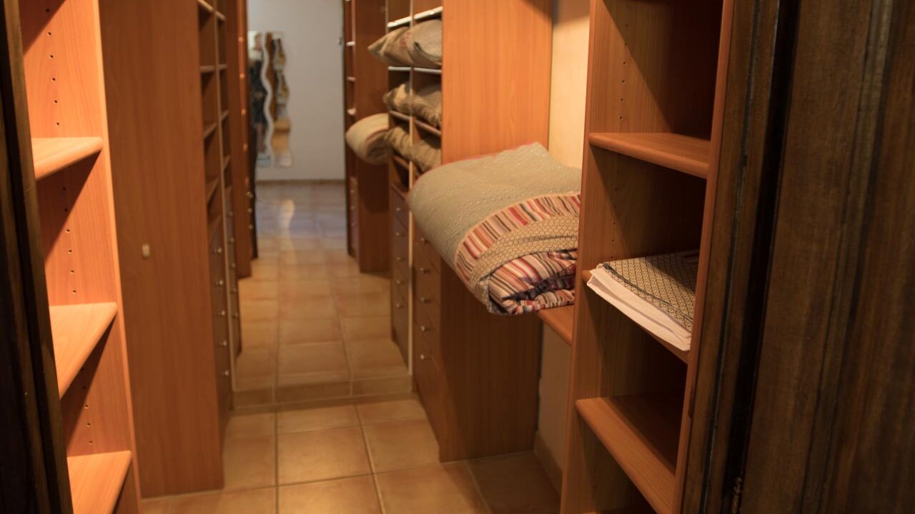 A narrow walk-in closet at Mas Saint Antoine, with wooden shelves on both sides holding folded blankets and linens, tiled floor, and a large mirror at the end reflecting the inviting space—perfect for groupe hébergement Ardèche méridionale. A narrow walk-in closet at Mas Saint Antoine, with wooden shelves on both sides holding folded blankets and linens, tiled floor, and a large mirror at the end reflecting the inviting space—perfect for groupe hébergement Ardèche méridionale.