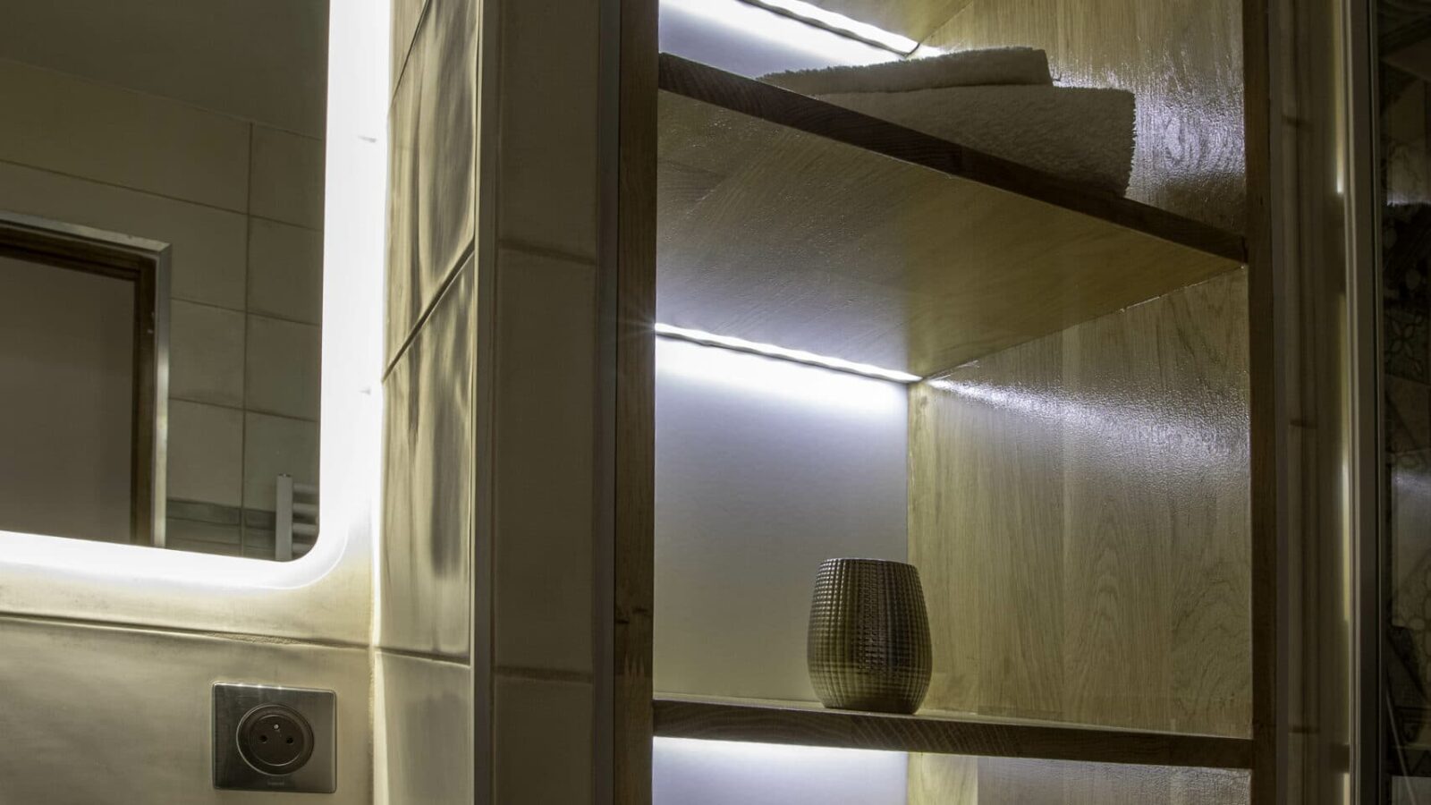 A wooden bathroom shelf with built-in lighting holds neatly folded white towels and a small decorative vase, creating a relaxing vibe reminiscent of Mas Saint Antoine, gîte Ardèche, just steps from the pool (piscine) and serene countryside views. A wooden bathroom shelf with built-in lighting holds neatly folded white towels and a small decorative vase, creating a relaxing vibe reminiscent of Mas Saint Antoine, gîte Ardèche, just steps from the pool (piscine) and serene countryside views.