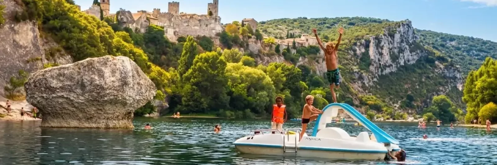 Des personnes profitent d'un bateau à aubes avec un toboggan sur une rivière calme près de falaises rocheuses et d'une végétation luxuriante ; une personne saute du toboggan tandis que d'autres regardent. Un village historique perché et le Mas Saint Antoine, un gîte de charme ardéchois, sont visibles en arrière-plan.