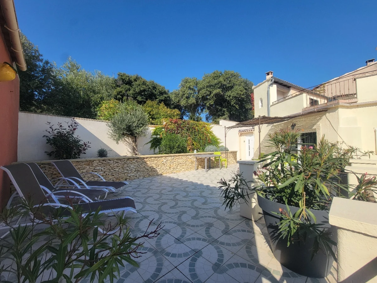 Terrasse provençale en galets d'un gîte du Mas Saint Antoine, transats et oliviers sous un ciel bleu, en Ardèche